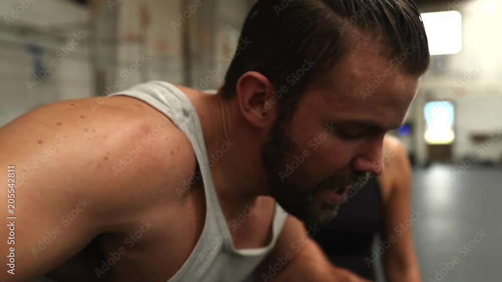 Closeup of a fit young man riding a stationary bike with a female friend shouting support during a workout session together at the gym Closeup of a fit young man riding a stationary bike with a female friend shouting support during a workout session together at the gym