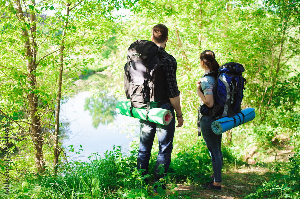 Fototapeta premium Young couple hikers in forest. sports man and woman with backpacks on road in nature