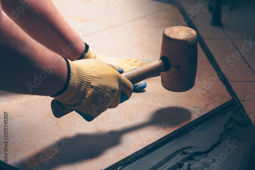 The working tiler knocks on the tile with a Tile Mallet, the professional checks the building level photo