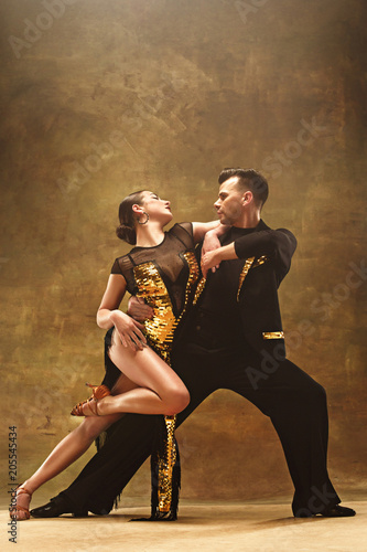 Tableau sur toile Dance ballroom couple in gold dress dancing on studio background.