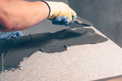 The hand of the working tiler puts a glue on the back of the ceramic tile with a spatula