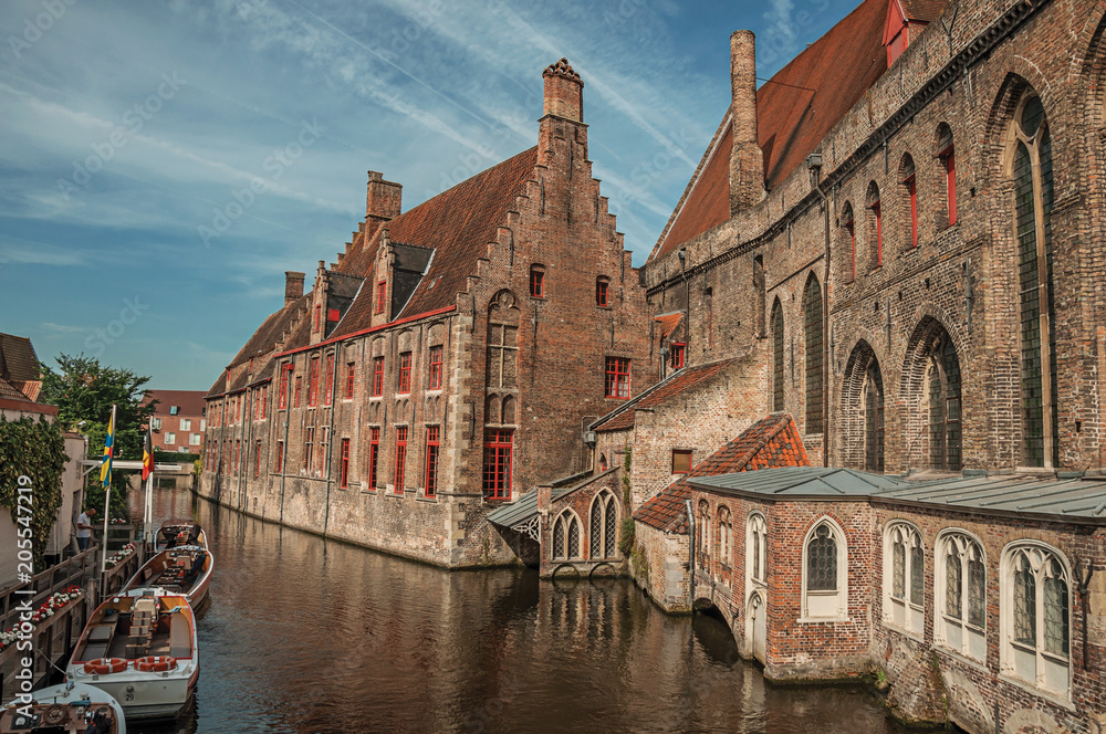 Old buildings on the canal bank, boats and sunny blue sky in Bruges. With many canals and old buildings, this graceful town is a World Heritage Site of Unesco. Northwestern Belgium.