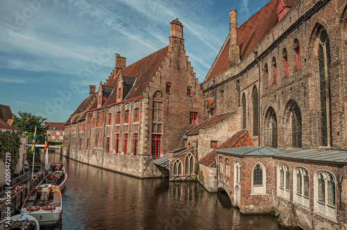 Old buildings on the canal bank, boats and sunny blue sky in Bruges. With many canals and old buildings, this graceful town is a World Heritage Site of Unesco. Northwestern Belgium.