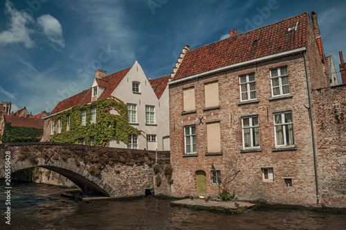 Bridge and brick buildings with creeper on the canal's edge in a sunny day at Bruges. With many canals and old buildings, this graceful town is a World Heritage Site of Unesco. Northwestern Belgium.