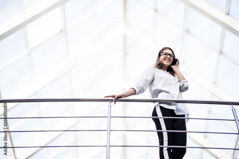 Confident business woman using mobile phone while leaning on railing in office