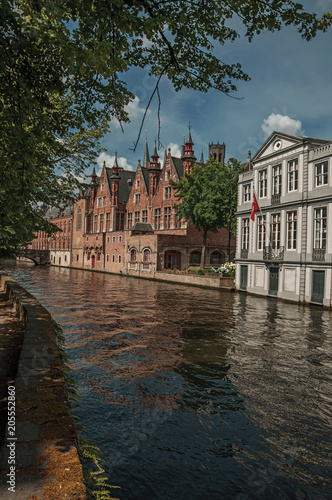 Wooded gardens and brick buildings on the canal's edge in a sunny day at Bruges. With many canals and old buildings, this graceful town is a World Heritage Site of Unesco. Northwestern Belgium.