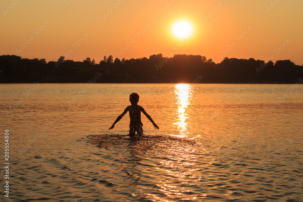 Young girl is playing in the water at sunset in summer. Golden sunset over the river