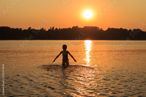 Young girl is playing in the water at sunset in summer. Golden sunset over the river