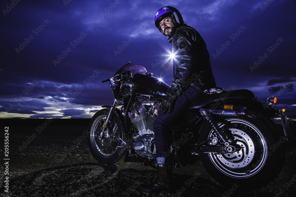 Modern biker turns on classic motorcycle at sunset with flash at back. Outdoor portrait and urban lifestyle Modern biker turns on classic motorcycle at sunset with flash at back. Outdoor portrait and urban lifestyle