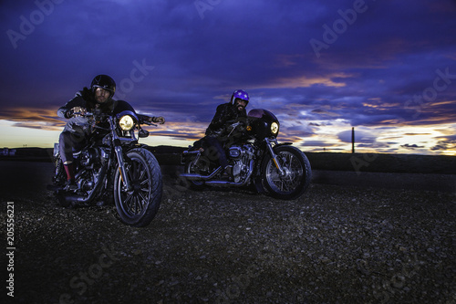 Modern bikers ride on a closed road with helmets on classic motorcycle at sunset. Outdoor portrait and urban lifestyle © Daniel