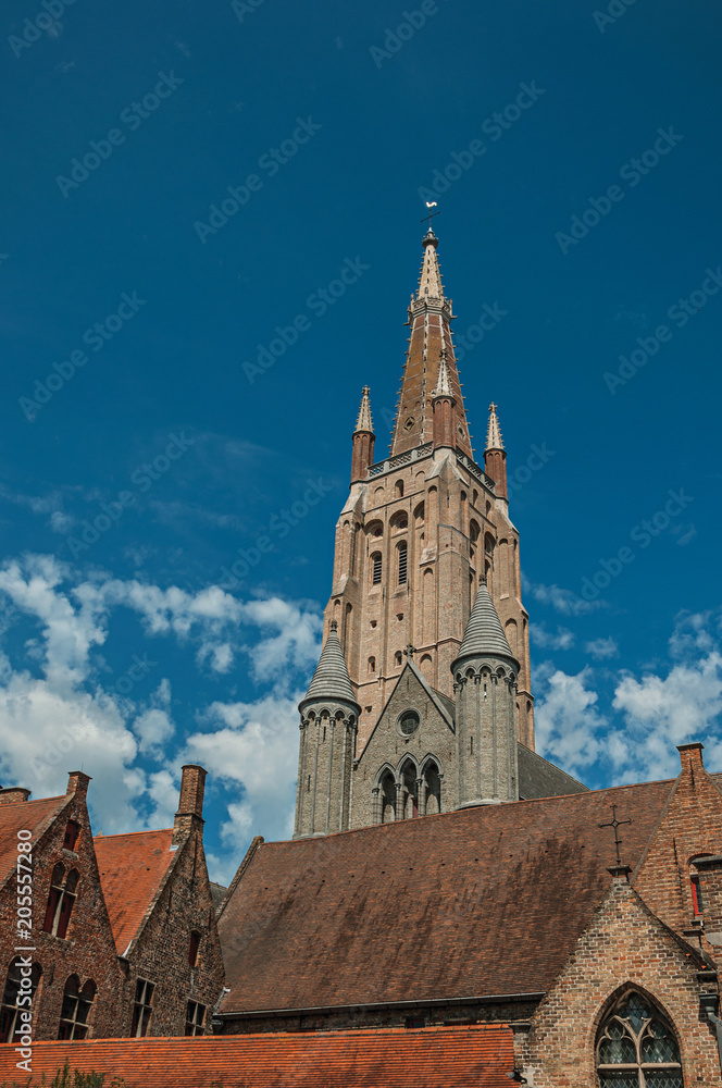 Brick church steeple, roofs and public lamp contrasting with blue sky in Bruges. With many canals and old buildings, this graceful town is a World Heritage Site of Unesco. Northwestern Belgium.