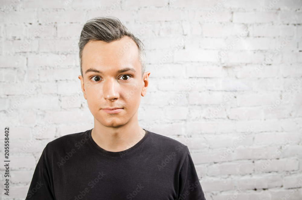 Young guy in black t-shirt with wide eyes looks in camera on brick wall backgound. Young guy in black t-shirt with wide eyes looks in camera on brick wall backgound.