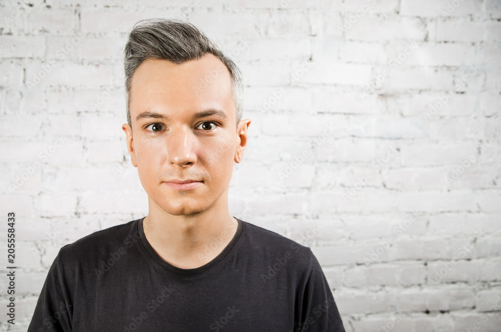 Young guy in black t-shirt with wide eyes looks forward on brick wall backgound. Young guy in black t-shirt with wide eyes looks forward on brick wall backgound.
