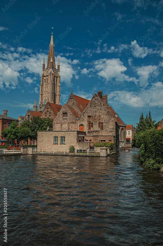 Steeple and old brick buildings on the canal's edge in a sunny day at Bruges. With many canals and old buildings, this graceful town is a World Heritage Site of Unesco. Northwestern Belgium.