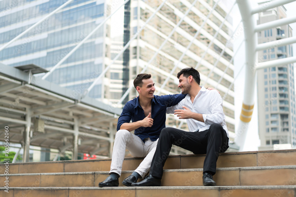 Two friend sitting down on stairs shaking hands. Businessmen very happy after success project. concept of business marketing, negotiation, compliment and management. Two friend sitting down on stairs shaking hands. Businessmen very happy after success project. concept of business marketing, negotiation, compliment and management.