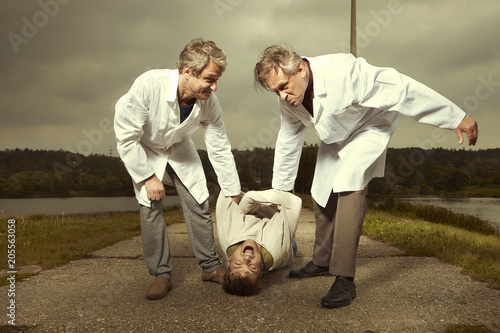 Fotografie Two older retro paramedic freak hunters in medical coats catching crazy man to s
