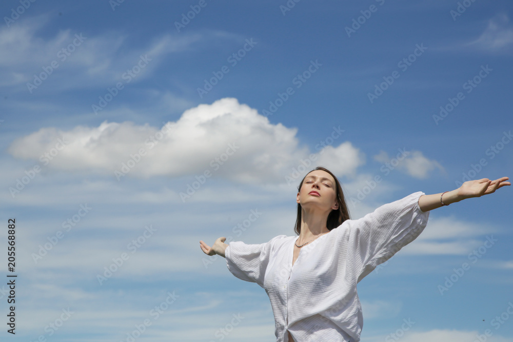 Young woman in white shirt with raised hands and fluffy sky background Young woman in white shirt with raised hands and fluffy sky background