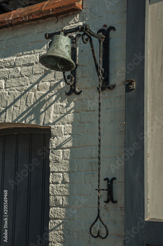 Close-up of bell pinned to wall facade of an old brick house, in the late afternoon light at Damme. A quiet and charming countryside old village near Bruges. Northwestern Belgium.