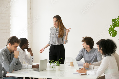 Angry caucasian female executive or team leader firing unprofessional african male employee for bad work or misconduct with hand gesture, diverse business people having conflict at group meeting