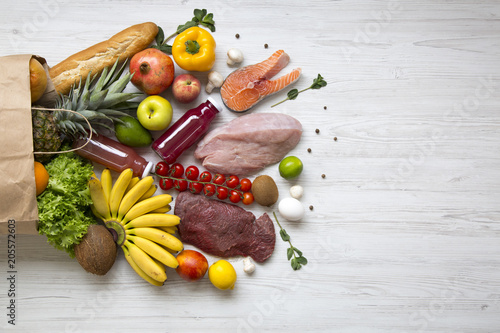 Paper bag of healthy raw food on white wooden table. Cooking food background. Flat-lay of fresh fruits, veggies, greens, different meat, top view, copy space. Shopping concept.