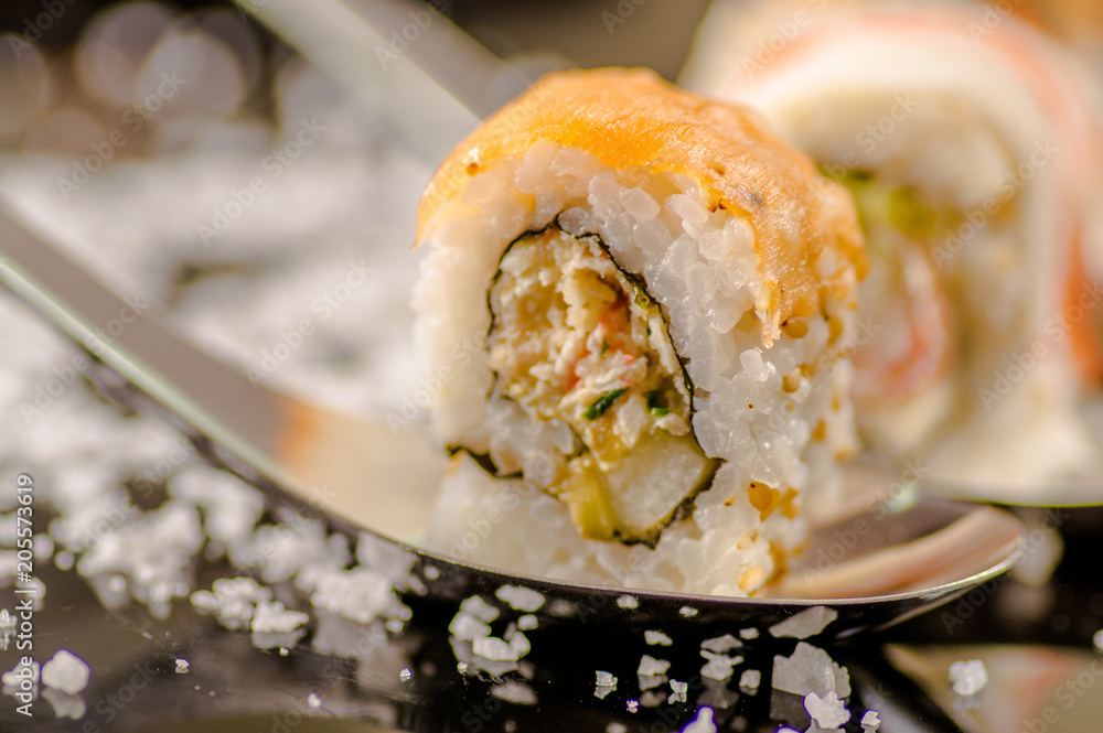 Close up of selective focus of delicious sushi rolls over a metallic spoon with small grains of salt served on black table Close up of selective focus of delicious sushi rolls over a metallic spoon with small grains of salt served on black table