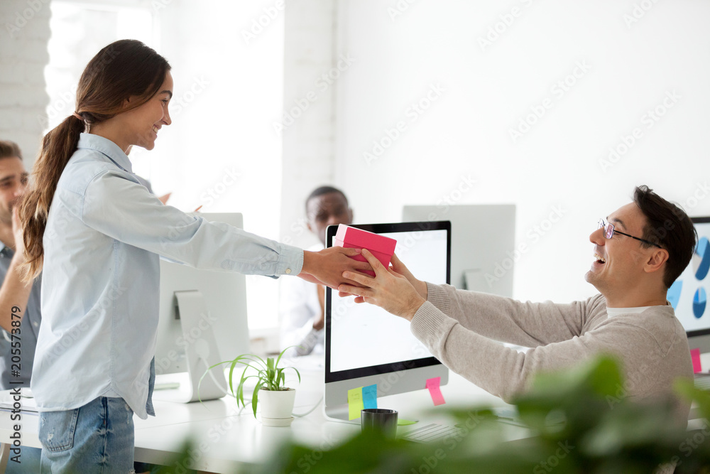 Obraz premium Friendly business team congratulating colleague making surprise present, smiling woman giving excited coworker or boss gift box, employees group greeting man wishing happy birthday in office concept