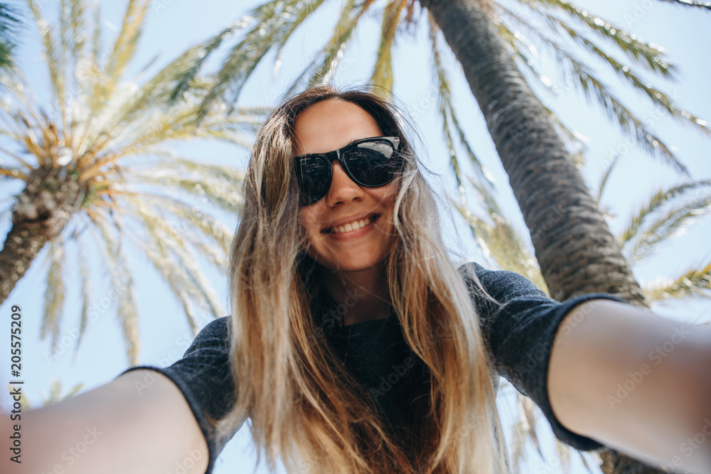 Young beautiful woman tourist or blogger makes a selfie or is reporting to its subscribers on the background of palm trees in a hot country Young beautiful woman tourist or blogger makes a selfie or is reporting to its subscribers on the background of palm trees in a hot country