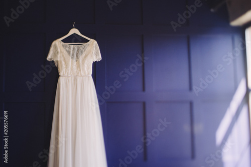 Wedding fashion. Bridal morning details. White lace dress hanging on blue wall.