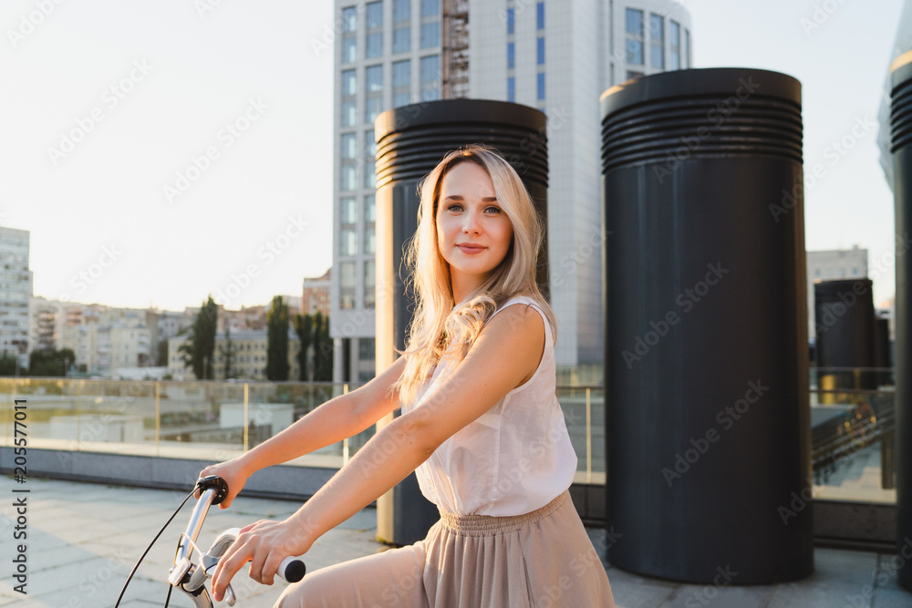 Lifestyle and health in the city. Active fashionable blonde smiling woman with vintage bike on urban background at sunset. Copy space. Good day for a ride.