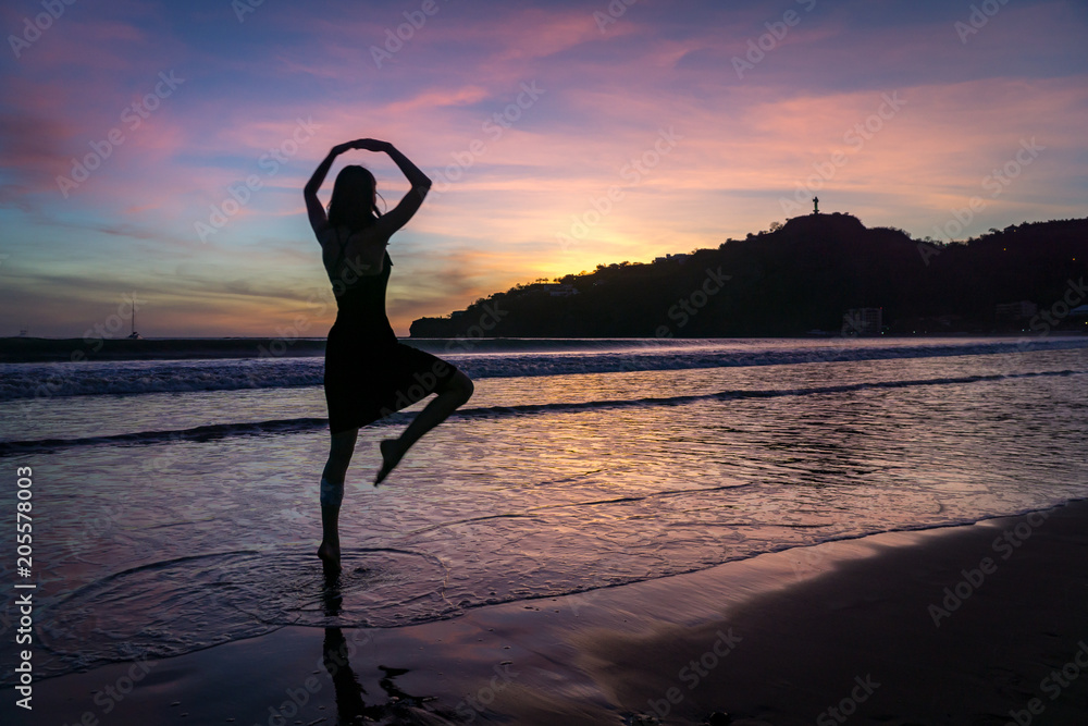 silhouette of woman practicing yoga on the beach at sunset.