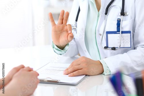 Doctor showing Ok sign to patient while sitting at the desk in hospital office, closeup of human hands. Medicine and health care concept