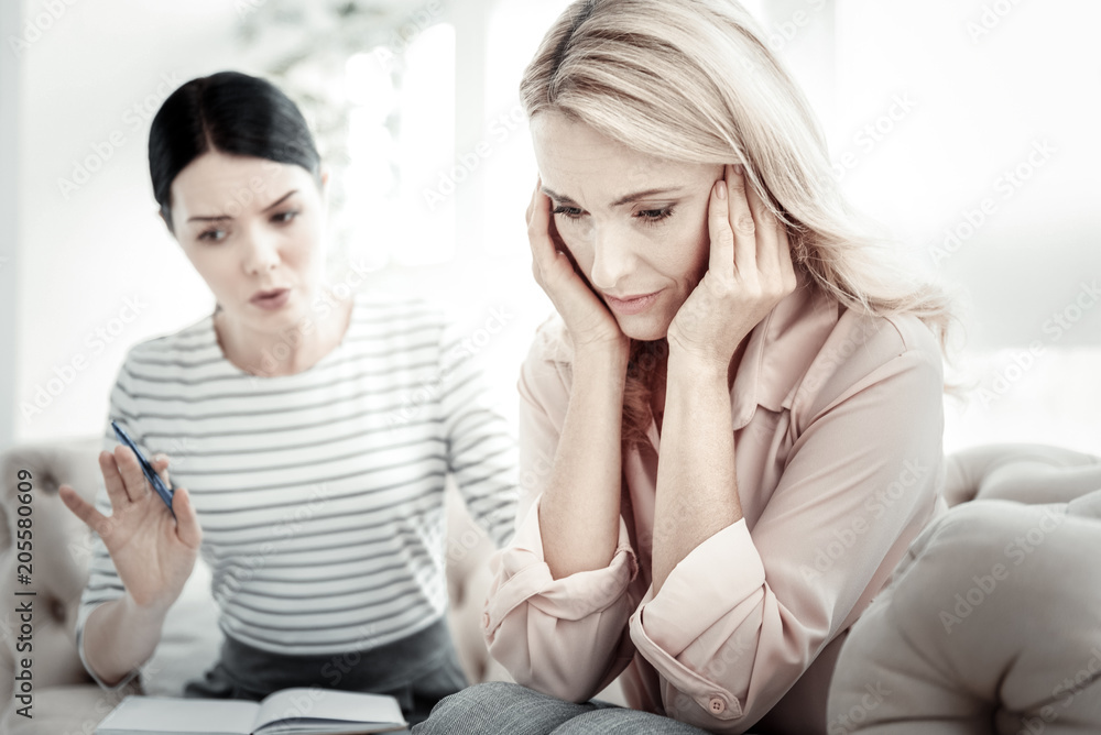 Just stop. Depressed disappointed exhausted woman sitting on the sofa near her friend looking down closing her ears by hands. Just stop. Depressed disappointed exhausted woman sitting on the sofa near her friend looking down closing her ears by hands.