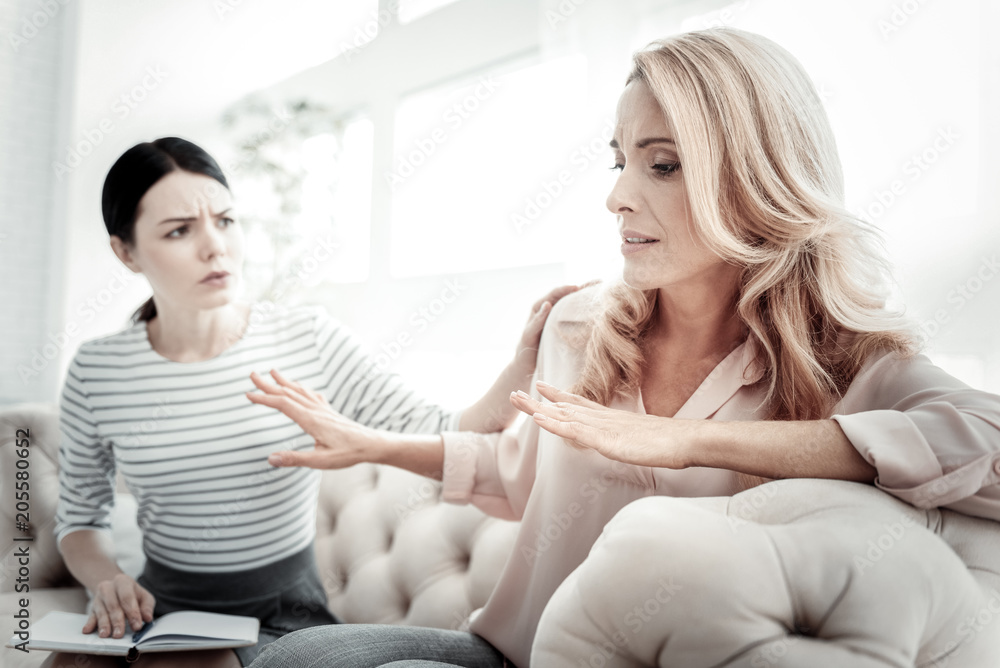 Dont want to hear. Unhappy disturbed tired woman communicating with her friend sitting near her on the sofa shaking her hands. Dont want to hear. Unhappy disturbed tired woman communicating with her friend sitting near her on the sofa shaking her hands.