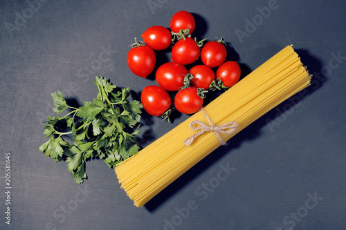 A bunch of pasta spaghetti with cherry tomatoes and parsley on a black background.