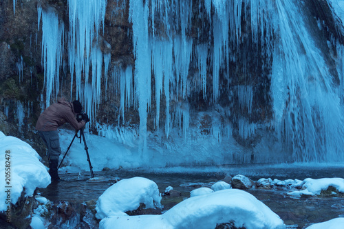 The photographer takes pictures of a frozen waterfall with a tripod