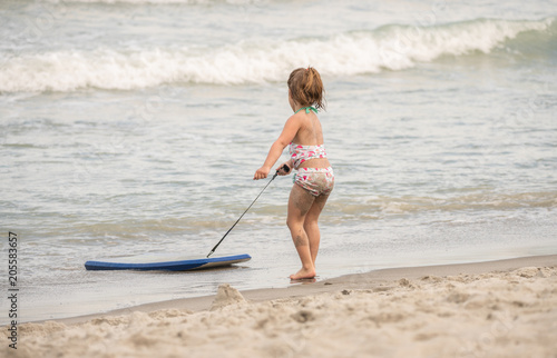 unknown little girl pulls her board to shore