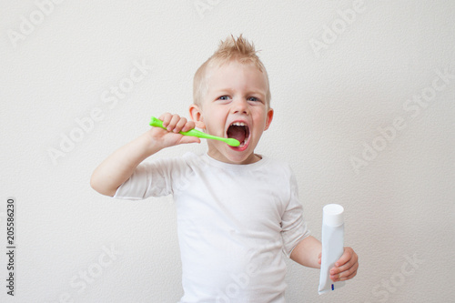 Little beautiful blonde kid boy brushing teeth. With toothpaste in hand. Health care, dental hygiene, people and beauty concept. photo