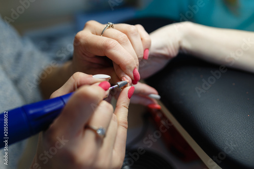 Closeup shot of hardware manicure in a beauty salon. Manicurist is applying electric nail file drill to manicure on female fingers. Manicurist takes off the manicure shellac with a nail client.