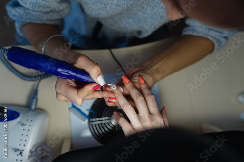 Closeup shot of hardware manicure in a beauty salon. Manicurist is applying electric nail file drill to manicure on female fingers. Manicurist takes off the manicure shellac. Top view