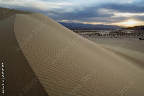 Sand dunes curve under a cloudy sky to create a dramatic landscape.