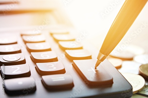 Business, finance, saving money, banking, loan, investment, taxes or accounting concept : Pen press on plus button calculator and coins on office desk table