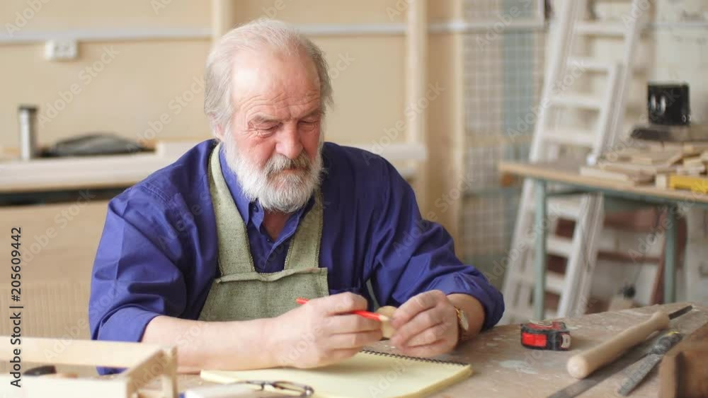 Old artisan in working outfit writing designing ideas. Old artisan in working outfit writing designing ideas.