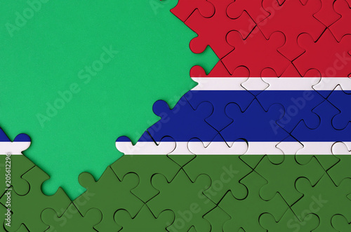 Gambia flag  is depicted on a completed jigsaw puzzle with free green copy space on the left side photo