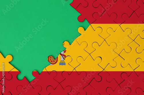 Spain flag  is depicted on a completed jigsaw puzzle with free green copy space on the left side photo