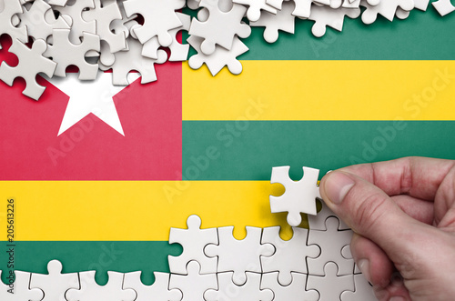 Togo flag  is depicted on a table on which the human hand folds a puzzle of white color photo