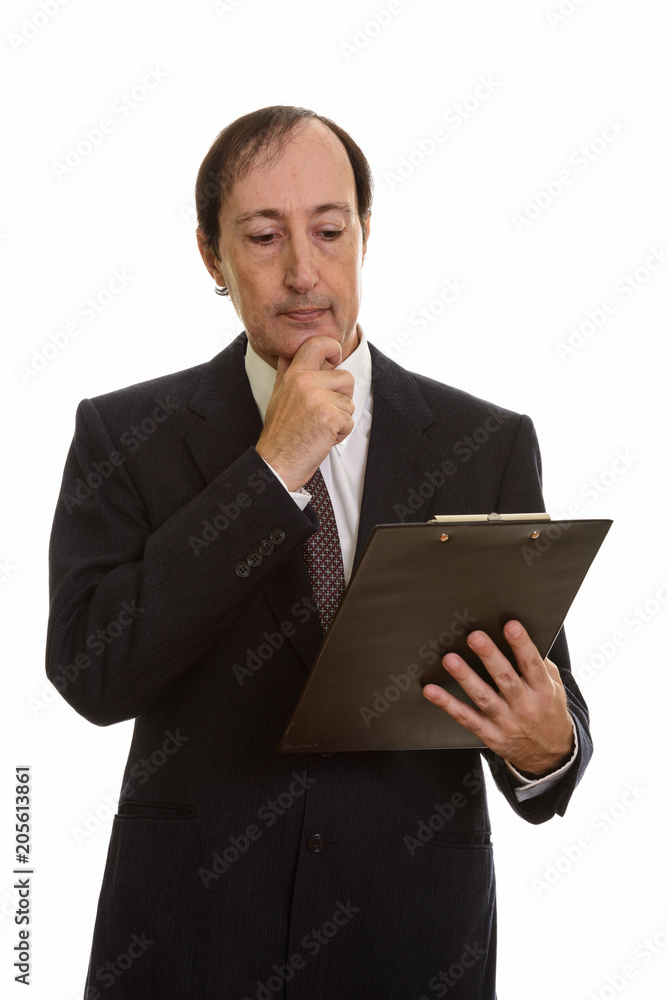 Studio shot of mature businessman reading on clipboard while thi Studio shot of mature businessman reading on clipboard while thi