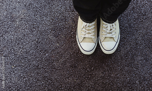 looking down at shoes on a bitumen surface with copy space beside it