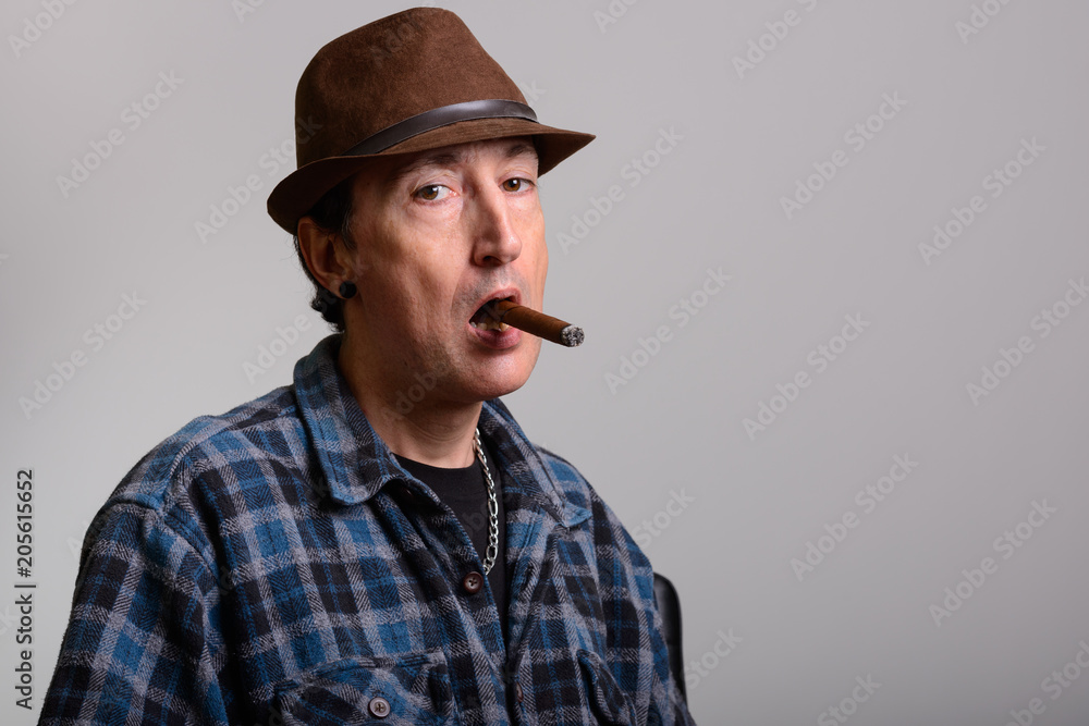 Studio shot of mature gangster man smoking cigar Studio shot of mature gangster man smoking cigar