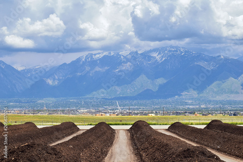 Rows of Compost ready for sale with Panoramic view of Wasatch Front Rocky Mountains, Great Salt Lake Valley in early spring with melting snow and Cloudscape. Utah. USA.