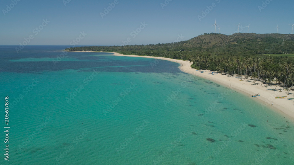 Aerial view of beautiful tropical beach Saud with turquoise water in blue lagoon, Pagudpud, Philippines. Ocean coastline with sandy beach and palm trees. Tropical landscape in Asia.